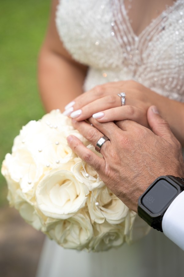Wedding rings and hands resting on a white rose bouquet
