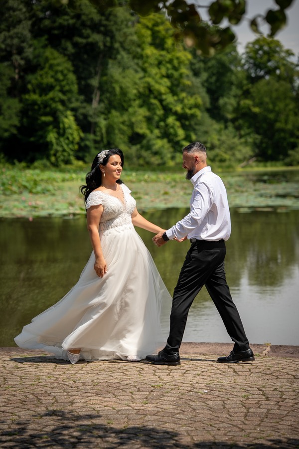 The couple holding hands as the bride turns by the water