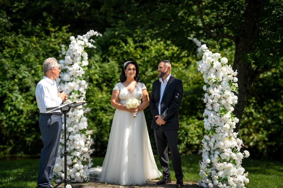 The couple standing beneath a white floral ceremony arch